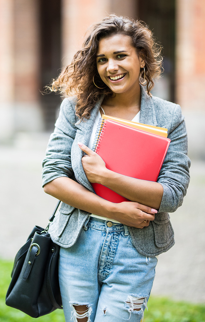 A CSUN student in jeans and a jacket holds a red folder, showcasing a casual yet professional appearance.