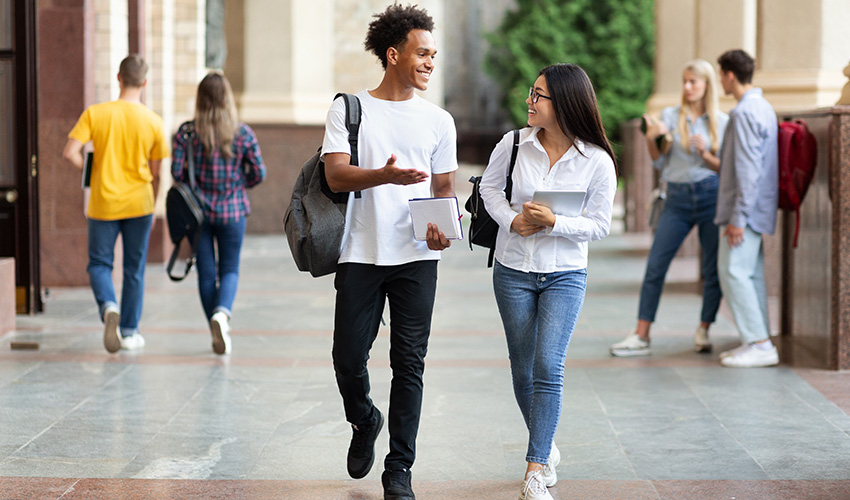 Two students walking side by side on a sidewalk, engaged in conversation and enjoying their time outdoors.