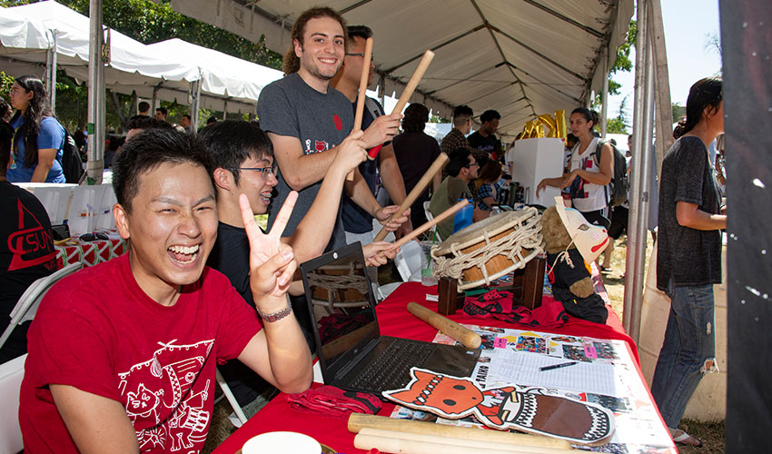 A group of students gathered around a table, enthusiastically playing various drums together.