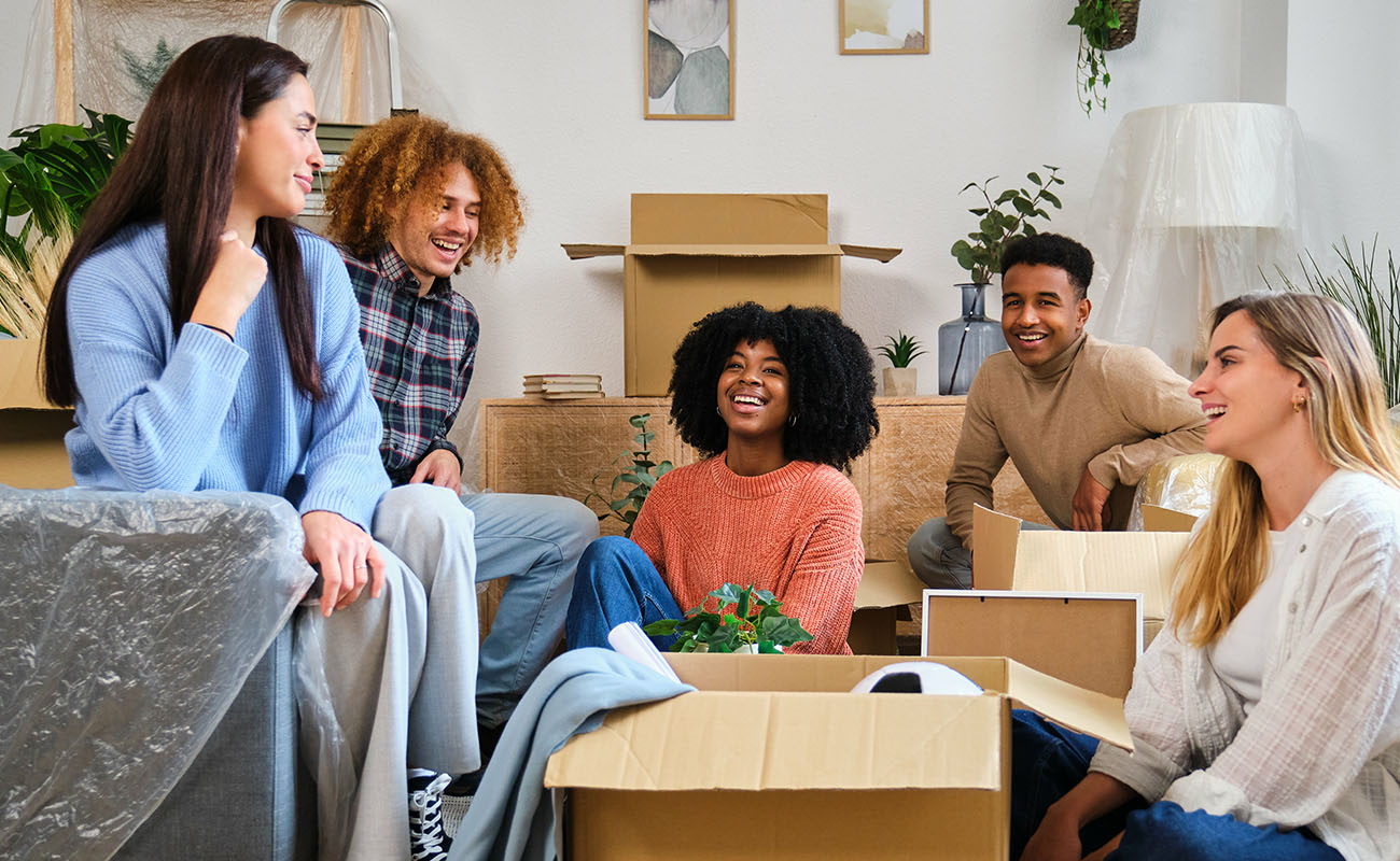 Students sitting together in a room filled with boxes, excitedly organizing their new student housing space.