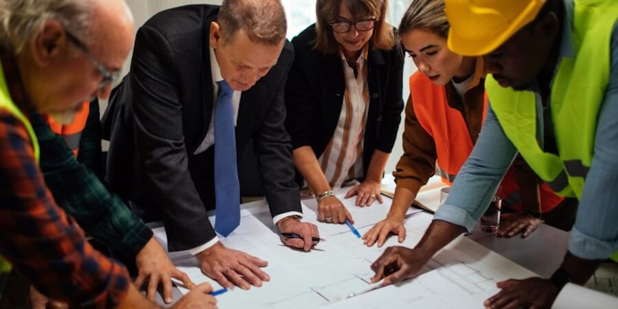 A director of engineering talking with staff members surrounding a table holding building plans.