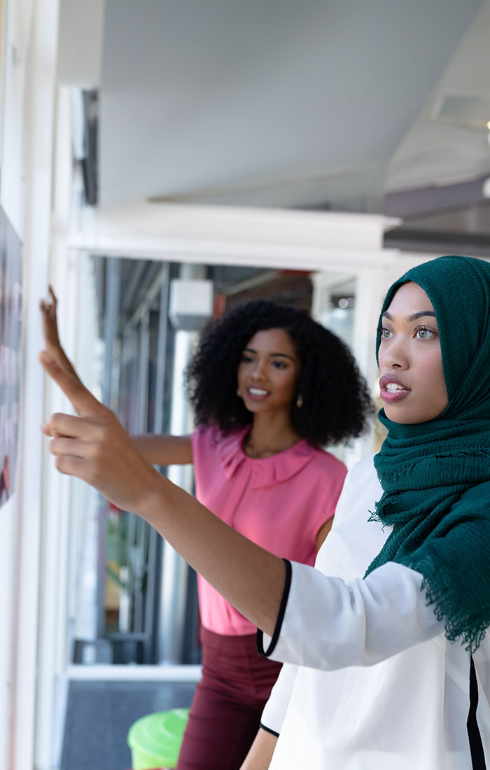 Two female professionals reviewing documents pinned to a whiteboard.
