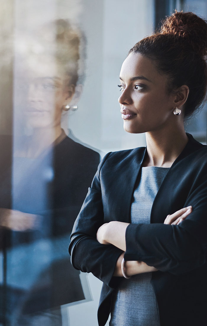 A woman in business attire looking out the window at her reflection.
