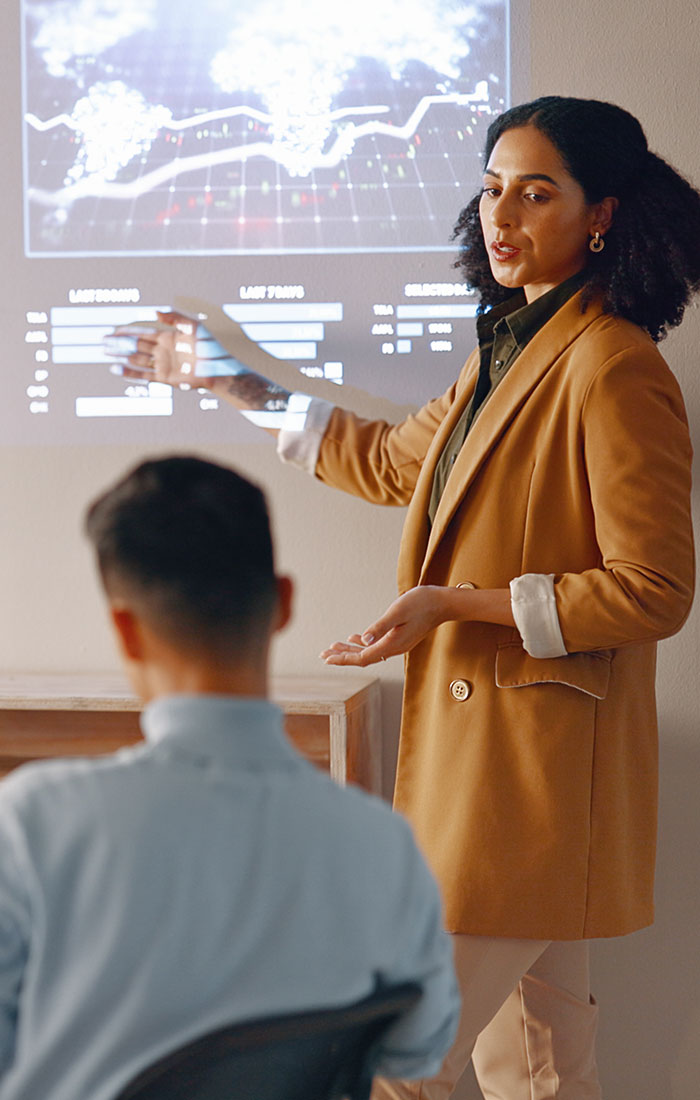 A person giving a presentation referencing data projcted on the wall.